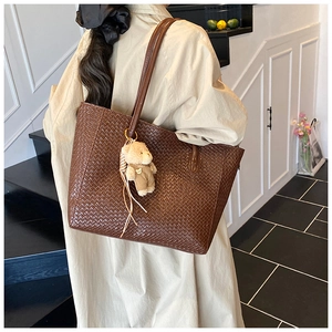 Close-up of deep brown woven tote bag with a plush bear charm on a female model
