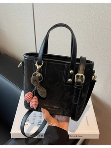 Chic black patent leather bucket bag with dual handles and tulip charm on a minimal background