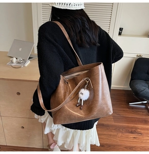 Detail view of retro brown leather tote bag with a white plush monster charm on the side