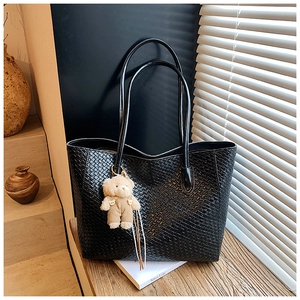 Macro shot of black woven leather tote bag texture with a cute plush bear charm detail