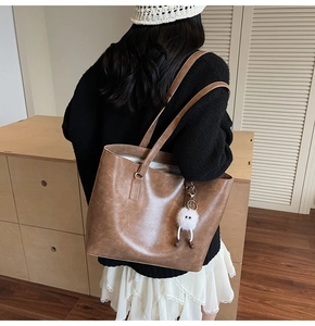 Detail of dark caramel tote bag with leather texture and white plush charm on strap