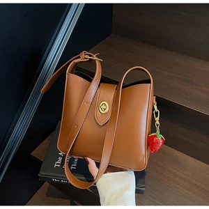 Detalle de bolso bucket de cuero marrón con cierre dorado y dije de fresa en escalera