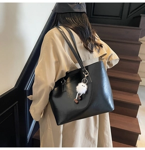 Minimalist black PU leather tote bag with white furry charm shown on shoulder