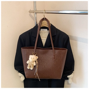 Detail of dark brown woven leather tote bag with a cute bear charm on a slim shoulder strap
