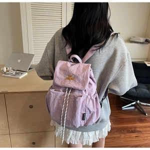 Close-up of light purple nylon backpack with drawstring flap and yellow embroidery detail