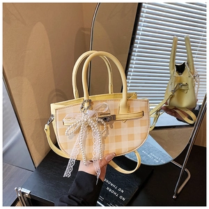 Detail of yellow plaid bucket bag featuring a large pearl lace bow and metal twist lock
