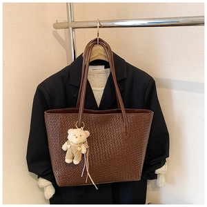 Detail of dark brown woven texture tote bag with cute plush bear charm hanging on handle