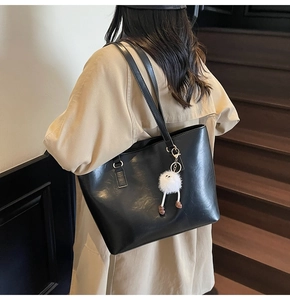 Detail of a black faux leather tote bag with a white plush charm on a wooden staircase