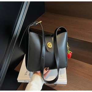 Detalle del bolso negro de cuero minimalista con cierre dorado y colgante de fresa roja