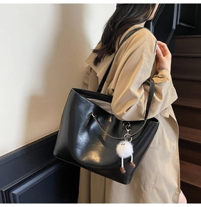 Close-up of black tote bag in PU leather with plush charm on beige interior background
