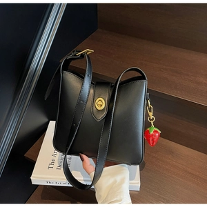 Detalle del bolso de cuero negro mate con cierre giratorio dorado y dije de fresa