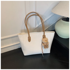 Detail of white woven tote bag with brown handles and a cute brown teddy bear charm