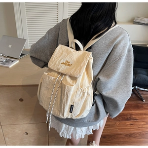 Close-up of the beige crinkled nylon backpack featuring orange YOU JI BEAR embroidery