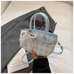 Detail of checkered Kelly-style bag with pearl bow charm and silver metallic hardware lock