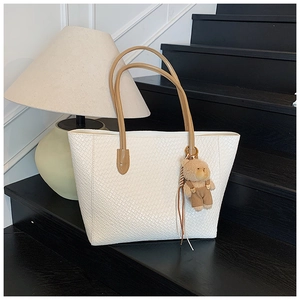 Detail of white woven tote bag with brown straps and a cute plush bear charm accessory