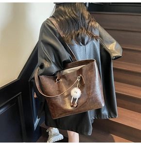 Detail view of deep brown vintage tote bag with oil wax leather texture and plush doll charm