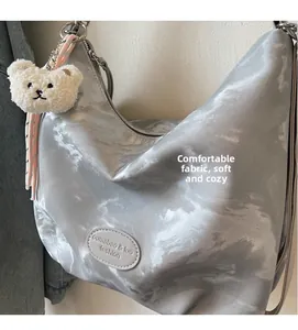 Dettaglio della grande borsa tote argento con texture morbida e ciondolo orsetto di peluche