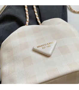 Detail der gewebten Karo-Beuteltasche mit goldener Kette und Logo-Plakette