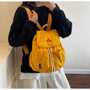 Detail of bright yellow drawstring backpack featuring red embroidery and stylish street style
