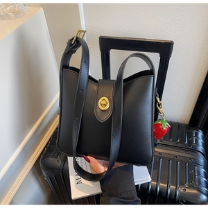 Detalle del bolso tipo cubo de cuero negro con cierre dorado y colgante de fresa en maleta