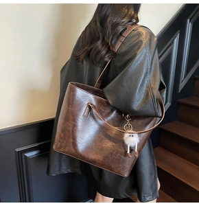 Large dark brown tote bag with vintage texture and white plush charm on model