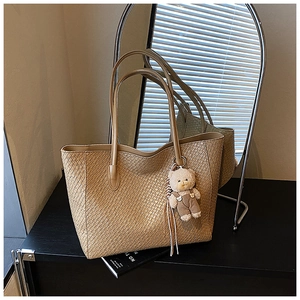 Detail of woven khaki tote bag featuring a cute beige bear plush charm and leather straps