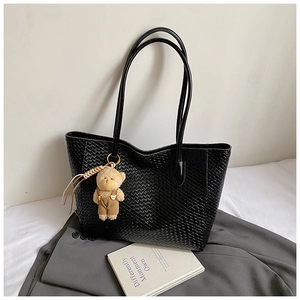 Close-up of black woven tote bag with a cute plush bear charm on a grey blazer background