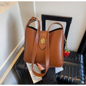 Detalle de bolso tipo cubo marrón con cierre dorado y un colgante de fresa decorativo