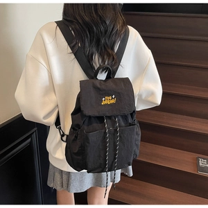 Close-up of black nylon backpack with yellow embroidery and drawstring closure detail