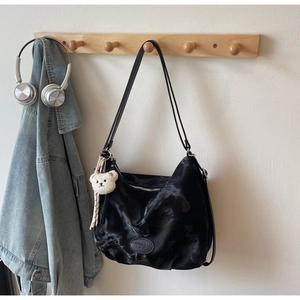 Dettaglio borsa hobo nera tie-dye con cuffie e un ciondolo a forma di orso di peluche
