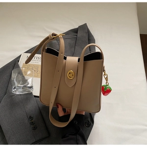 Detalle de bolso tipo cubo de cuero beige con cierre dorado y accesorio de amuleto de fresa
