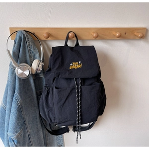 Detail of black nylon backpack with yellow embroidery hanging next to a denim jacket