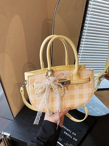 Yellow plaid bucket bag with a lace pearl bow charm and leather handle in a studio setting