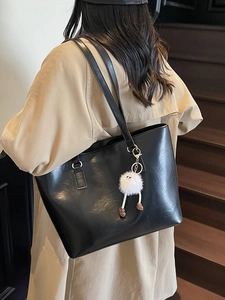 Minimalist black faux leather tote bag with white plush charm on a khaki trench coat