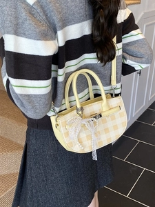Fashionable yellow plaid mini bucket bag with pearl bow charm worn as a crossbody bag