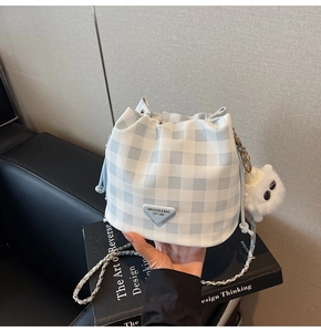 Detail der hellblauen Gingham-Beuteltasche mit Logo-Plakette und flauschigem Bommel