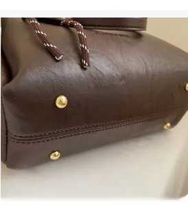 Close-up of deep brown leather bag bottom with four gold protective metal feet studs