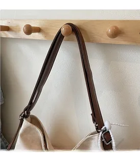 Close-up of off-white canvas tote bag featuring brown leather strap and metal buckle