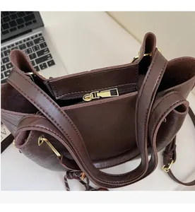 Close-up of smooth light gold zipper and top handle detail on brown leather bucket bag