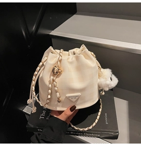 Nahaufnahme der beigen gesteppten Eimertasche mit Kettenriemen und Plüschanhänger