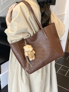 Brown woven faux leather tote bag with bear charm shown on a shoulder in a stylish setting