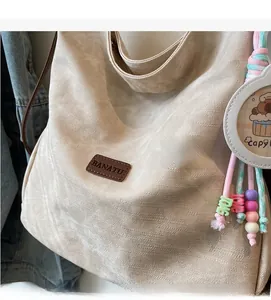 Close-up of beige canvas tote bag with brown leather logo and colorful beaded pendant