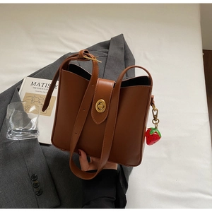 Detalle de bolso cubo de cuero marrón con cierre giratorio dorado y un colgante de fresa