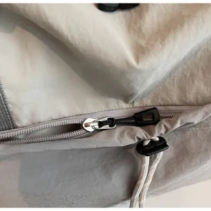 Detail view of smooth metal zipper and adjustable drawstring on gray nylon travel bag