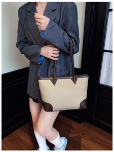 Detail of color-block tote bag with pebble leather and woven handles on a gray blazer
