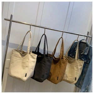 Detail view of large canvas tote bags in four colors hanging on a metal clothing rack