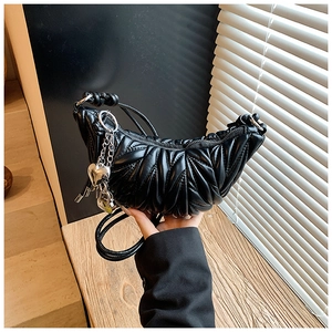 Détail d'un sac hobo matelassé noir avec pendentif cœur sur un support en bois