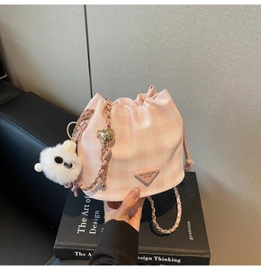 Detail der rosa karierten Beuteltasche mit Plüschanhänger und goldener Kette auf Buch