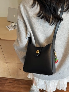 Bolso cubo retro de cuero negro con cierre dorado y colgante de fresa en mesa