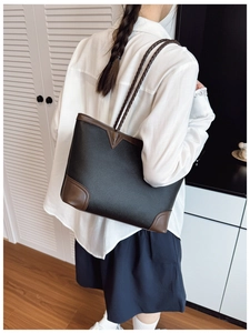 Detail of a large color-block tote bag with woven brown handles worn by a female model